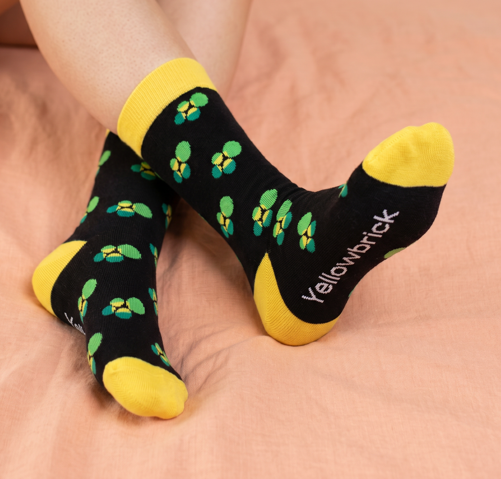 Close-up of a person's legs and feet wearing black socks with green and yellow lemon patterns and yellow toes and bands, on a pink background.