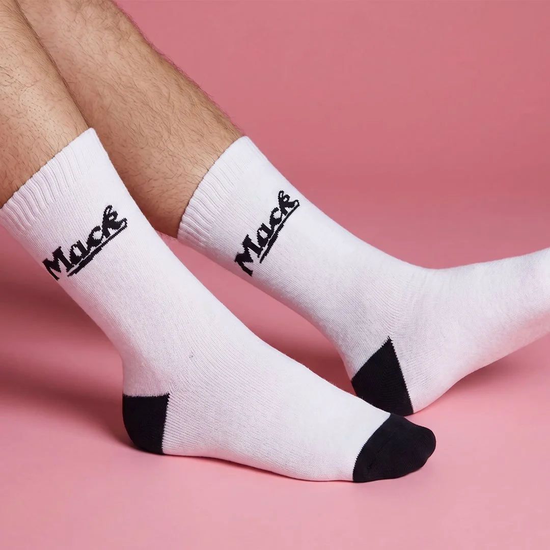 Person wearing white socks with black toe and heel areas, and the word "MARS" written on the side, against a pink background.