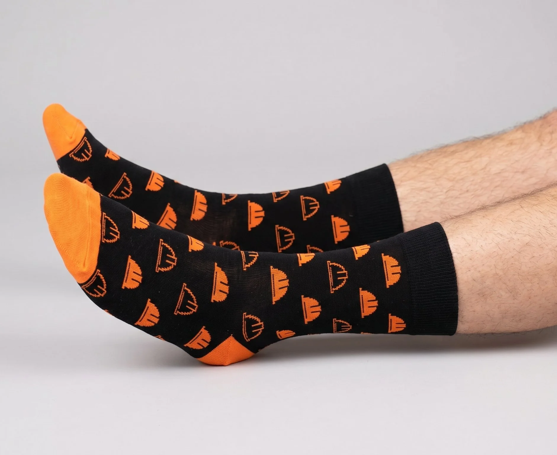 Black bamboo business socks with orange heel and toe, and orange helmets repeated over the sock