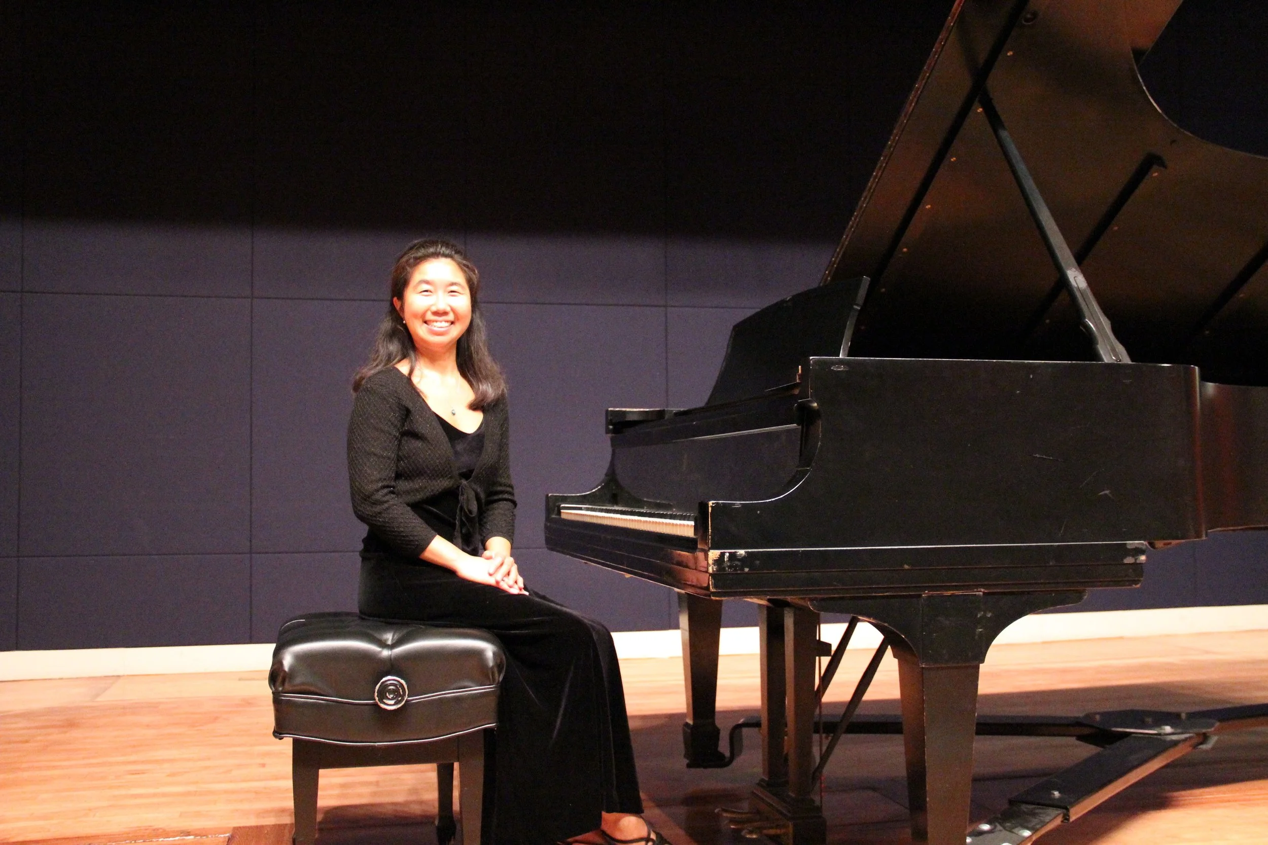 A photo of Natalie Warren sitting by the piano at a concert performance setting
