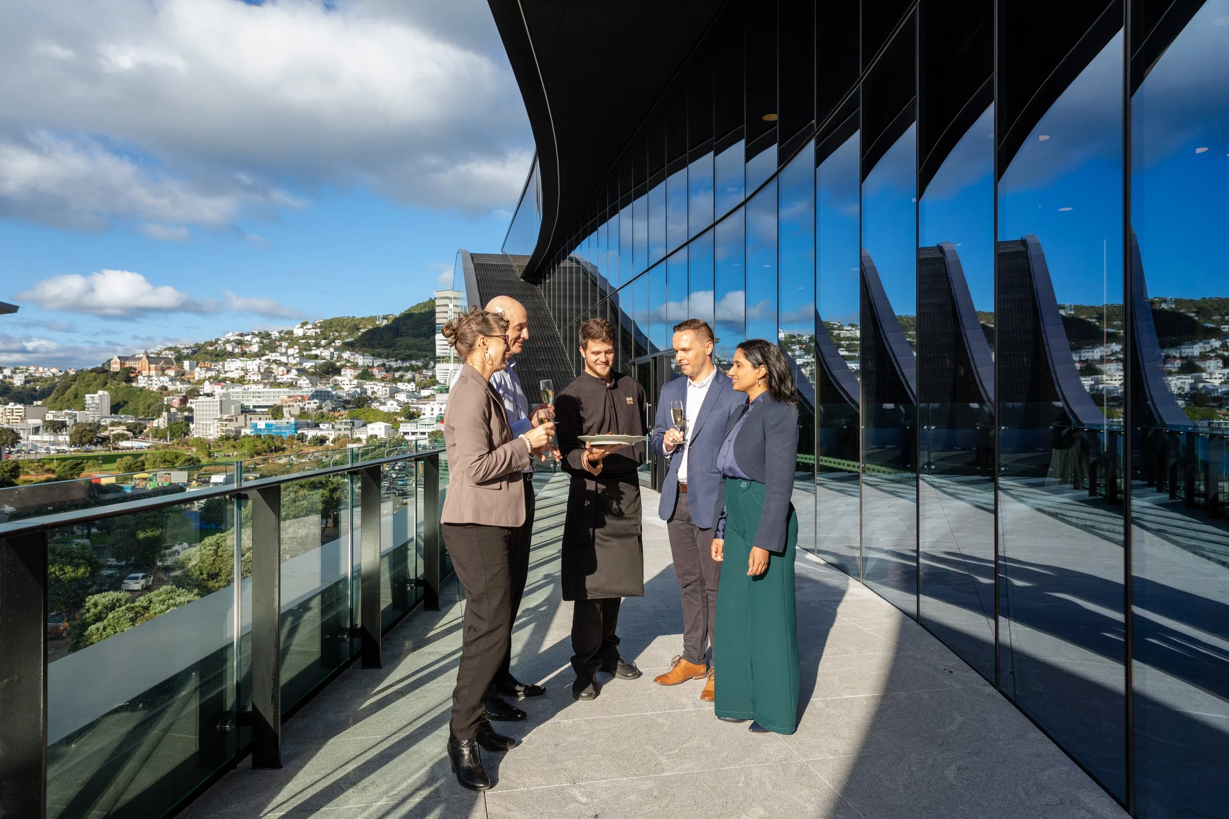 Business professionals networking on the balcony of Tākina Wellington Convention and Exhibition Centre overlooking Wellington city.