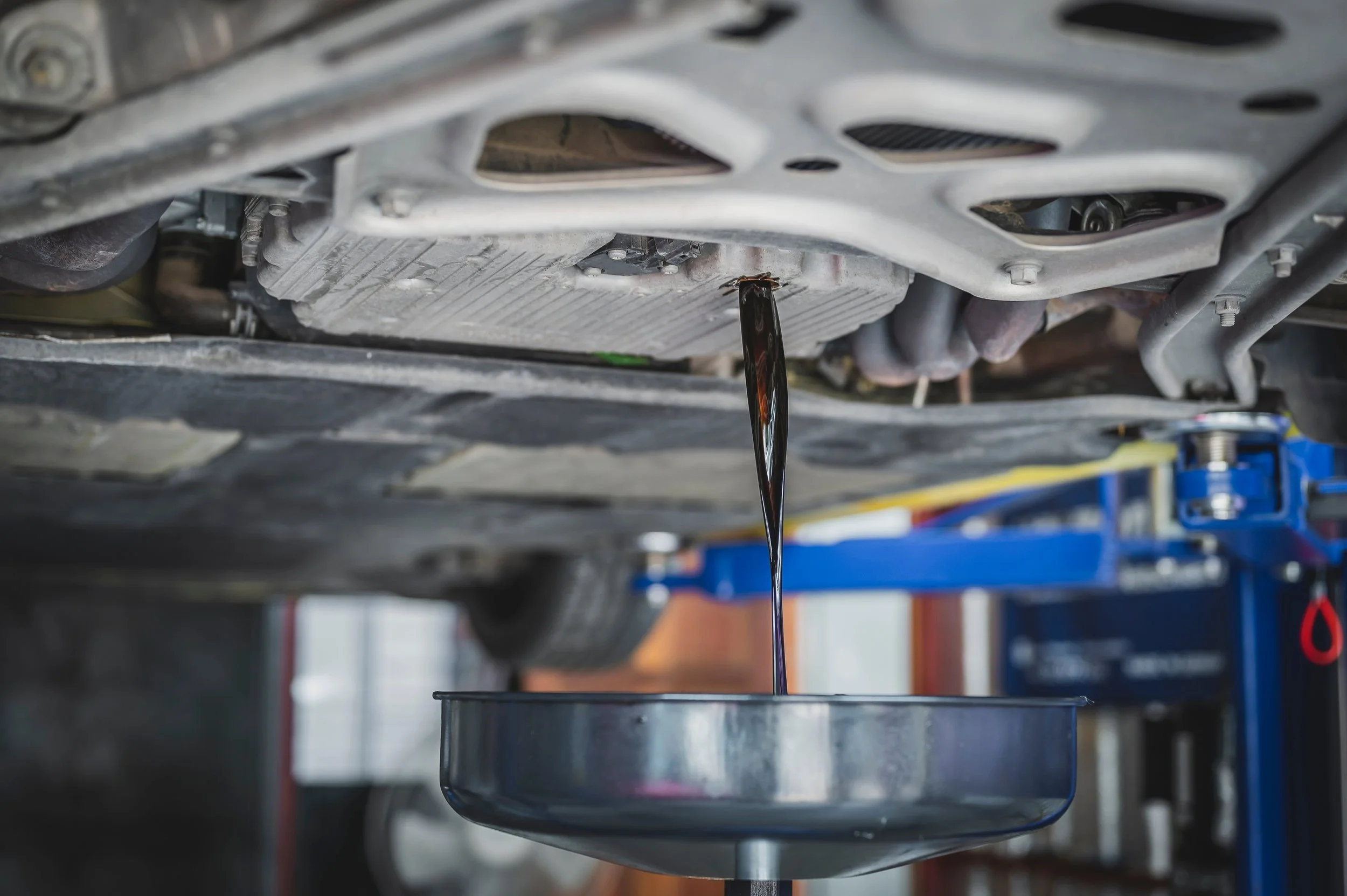 Car oil draining from the vehicle into a pan underneath the car's underside.