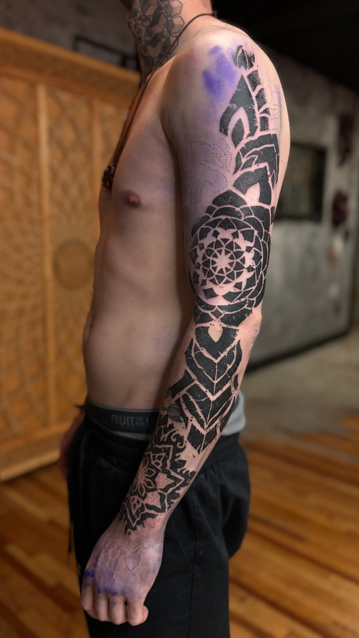 Person with a sleeve tattoo featuring geometric and floral designs on their arm, tattooed across the shoulder and forearm.