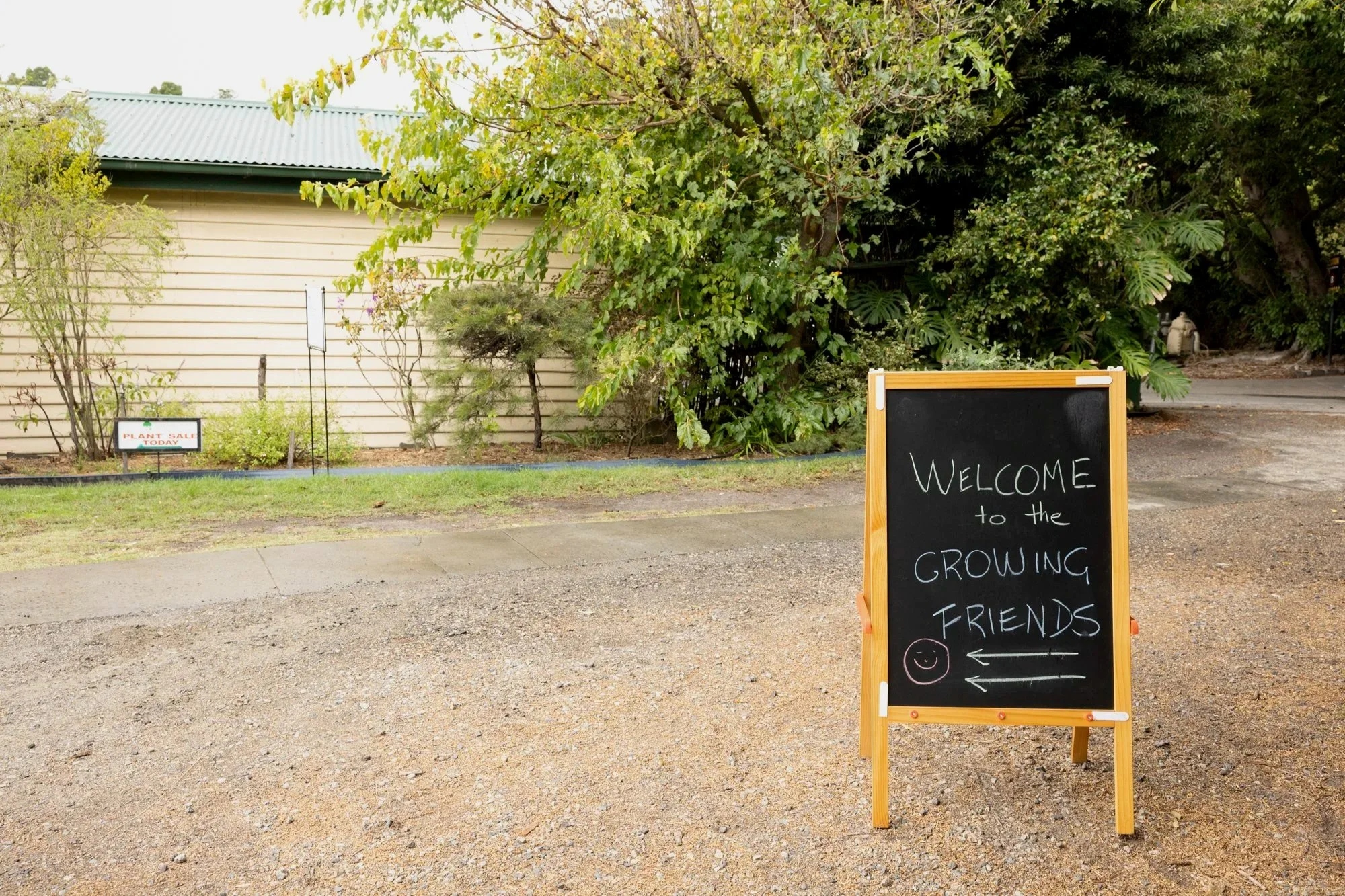 A handwritten note on a chalkboard sign shows the way to the Growing Friends nursery. It is written in coloured chalk with a smiley face and arrows.