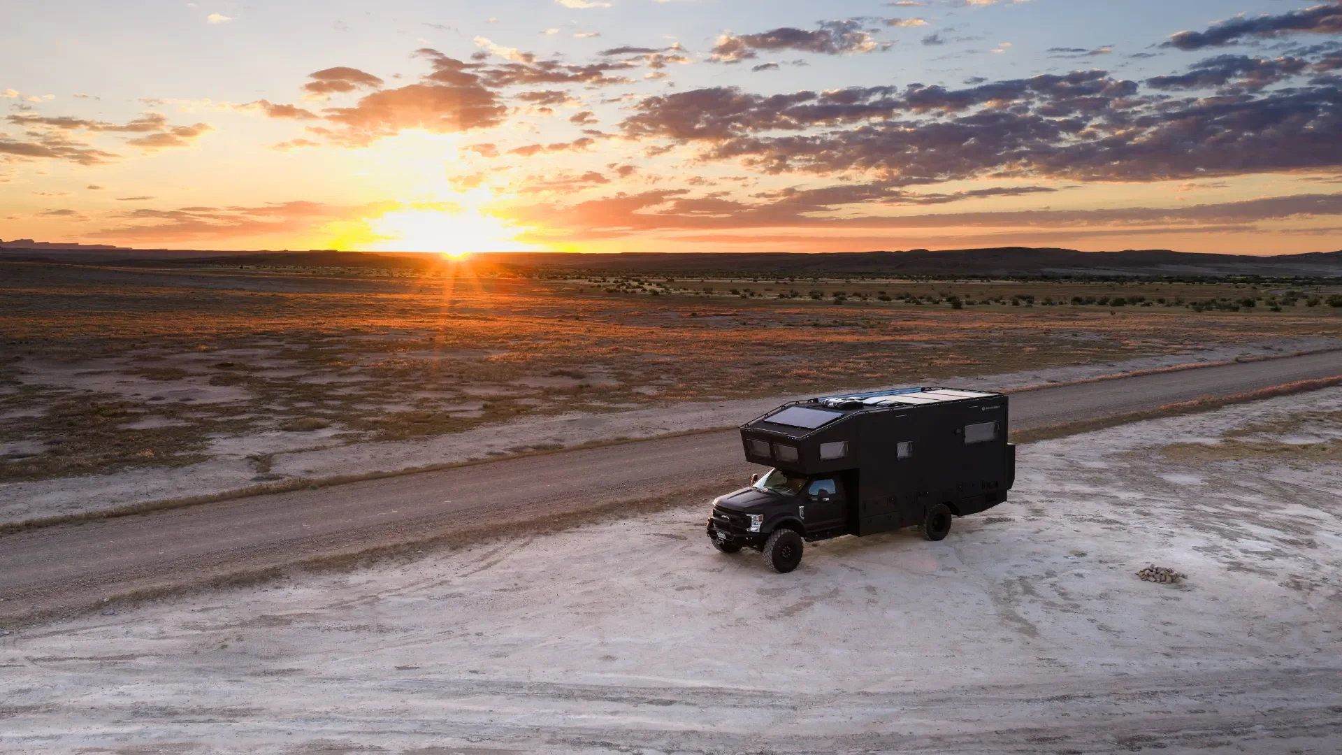 Aerial view of Emma's expedition RV crossing a desert plain at sunset
