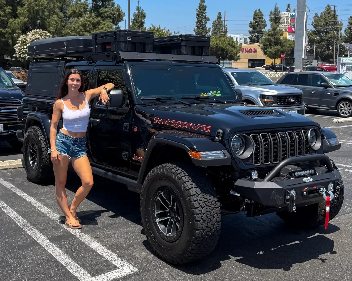 Emma Sinclair beside her black Jeep Gladiator with rooftop tent
