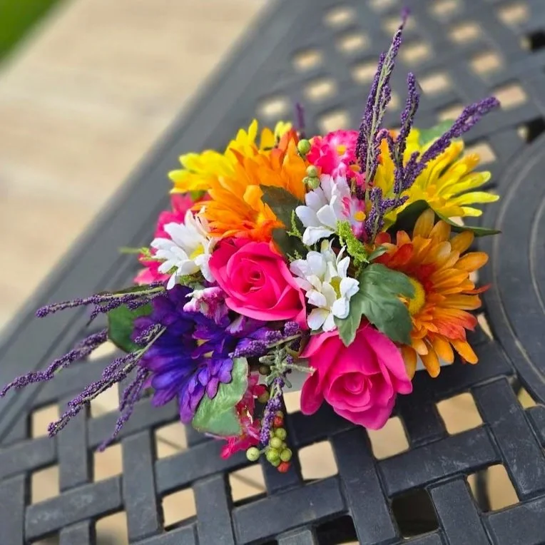 Colorful bouquet of pink roses, yellow, orange, purple, and white flowers with green leaves on a black outdoor table.