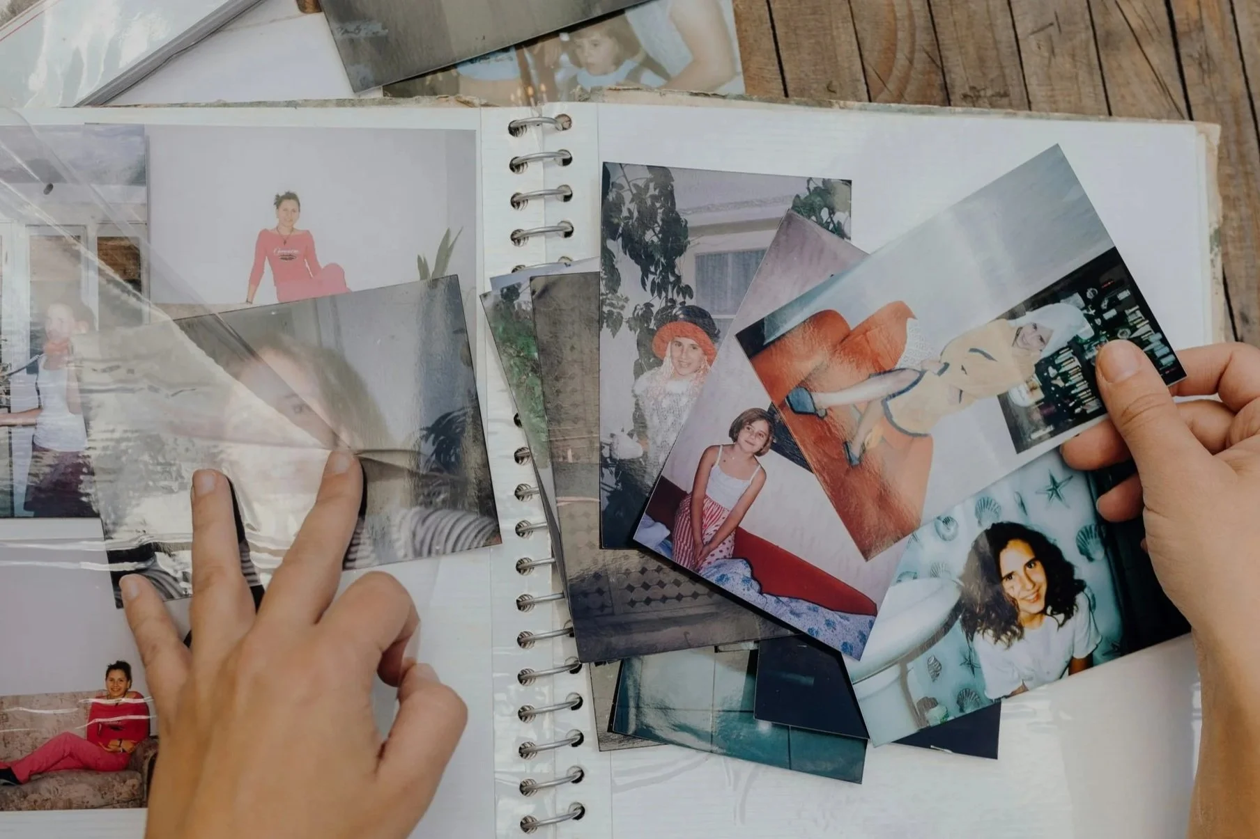 Hands holding and organizing small printed photographs on a white surface with a notebook underneath.
