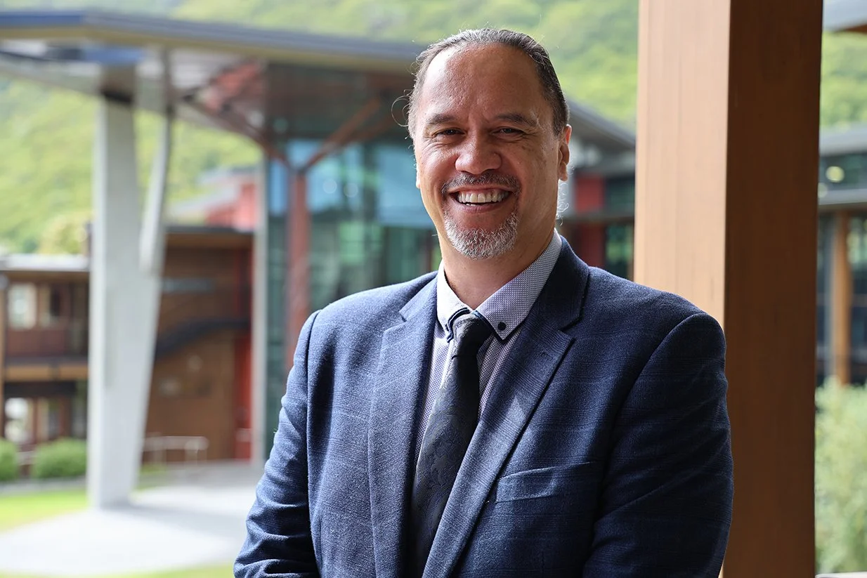 Portrait of a smiling Katoa Connect team member standing outdoors in front of a modern building, wearing a navy suit and tie.