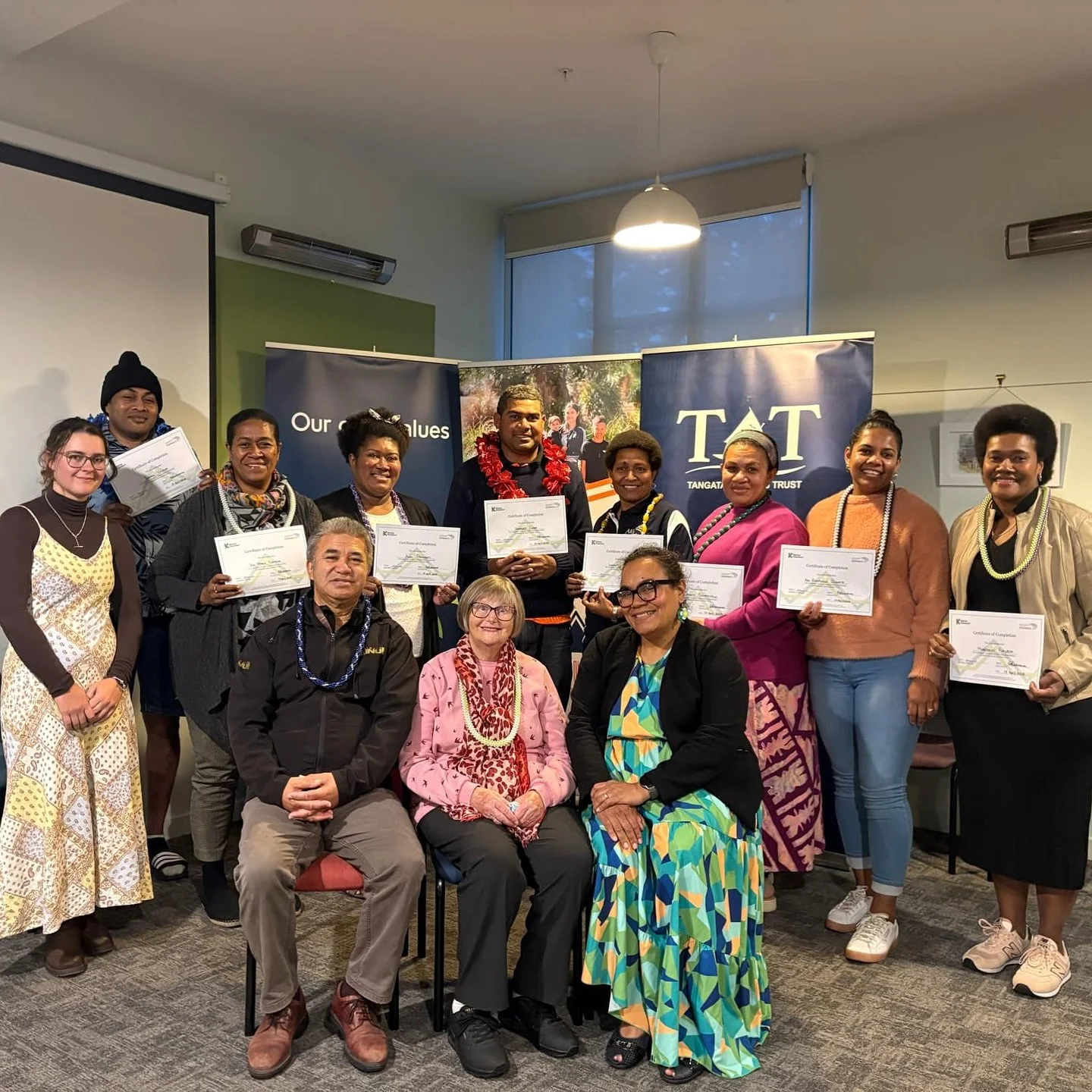 A group of people gather indoors holding certificates beside banners, celebrating achievement through a Katoa Connect programme. The image reflects community success, learning, and shared opportunity.