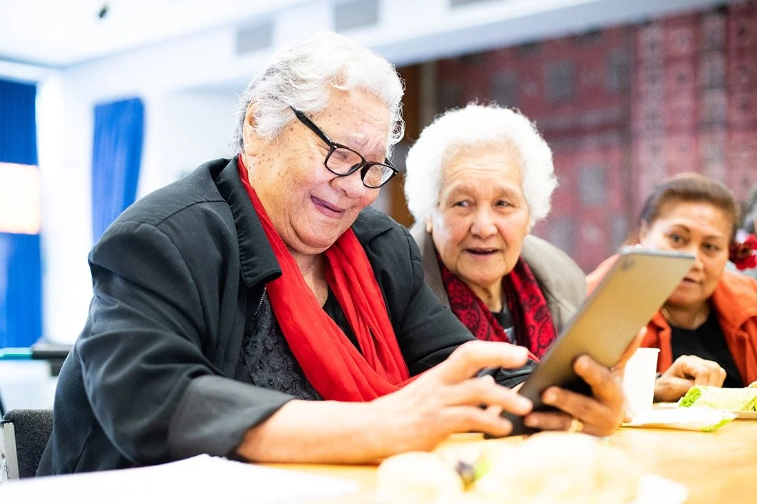 Katoa Connect image of three women gathered around a tablet, sharing a warm moment of digital learning, connection, and support in a community setting.