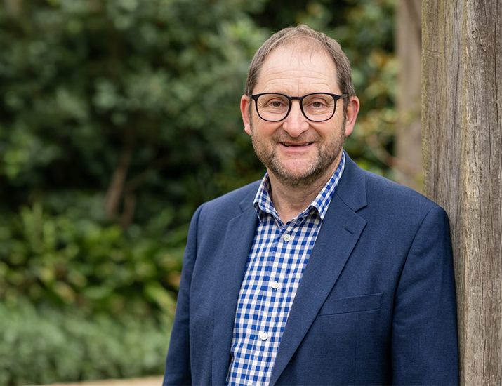 Craig Young, Katoa Connect Trustee, smiling outdoors in a professional portrait with a natural garden setting in the background.