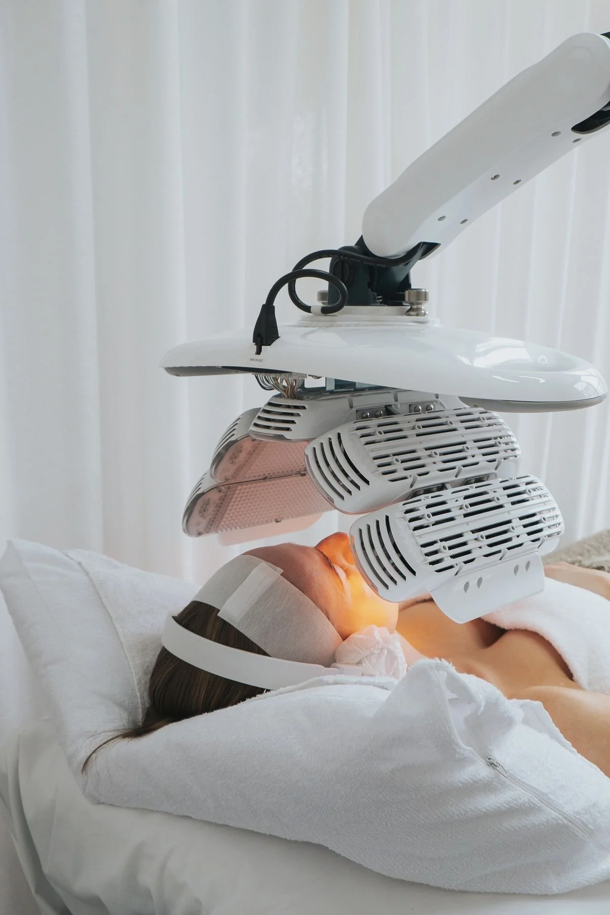 A person lying on a treatment bed undergoing laser hair removal with a large laser device positioned over their face.