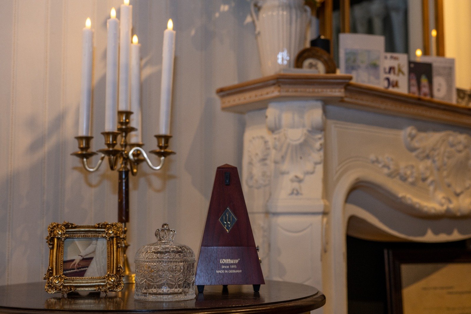 A mantelpiece with decorative items, a metronome, with a candelabra holding five lit candles beside it.