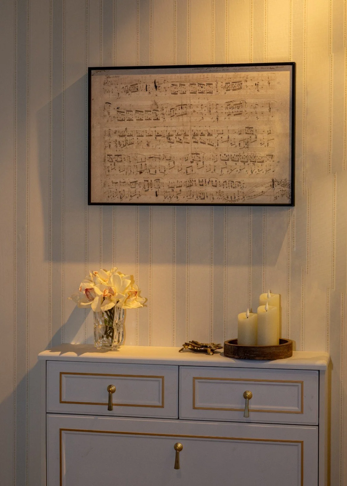 A framed autograph of Chopin's Heroic Polonaise hangs on a striped wall above a white dresser.