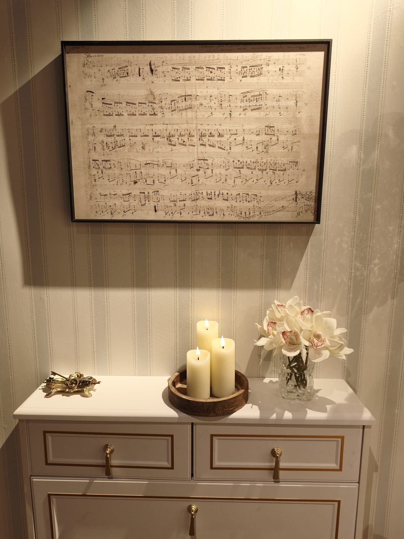 A framed autograph of Chopin's Heroic Polonaise hangs on a striped wall above a white dresser.