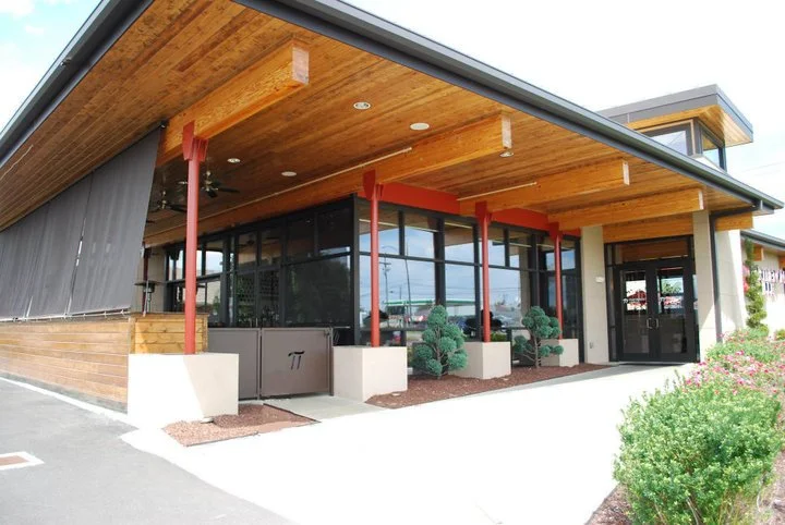 Modern commercial architecture and design featuring large glass windows, wooden overhang, and landscaping including bushes and flowers by Burke Architecture & Design Associates for Parthenon Grille in Murfreesboro, TN.