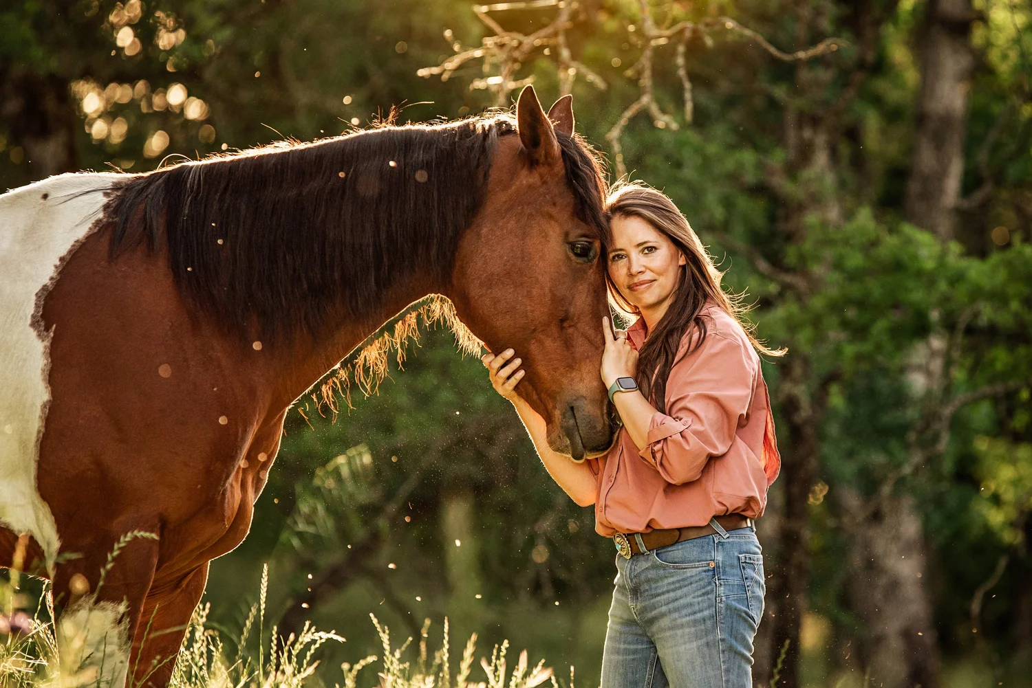Riece smiling, cheek to cheek with a paint horse in golden evening light