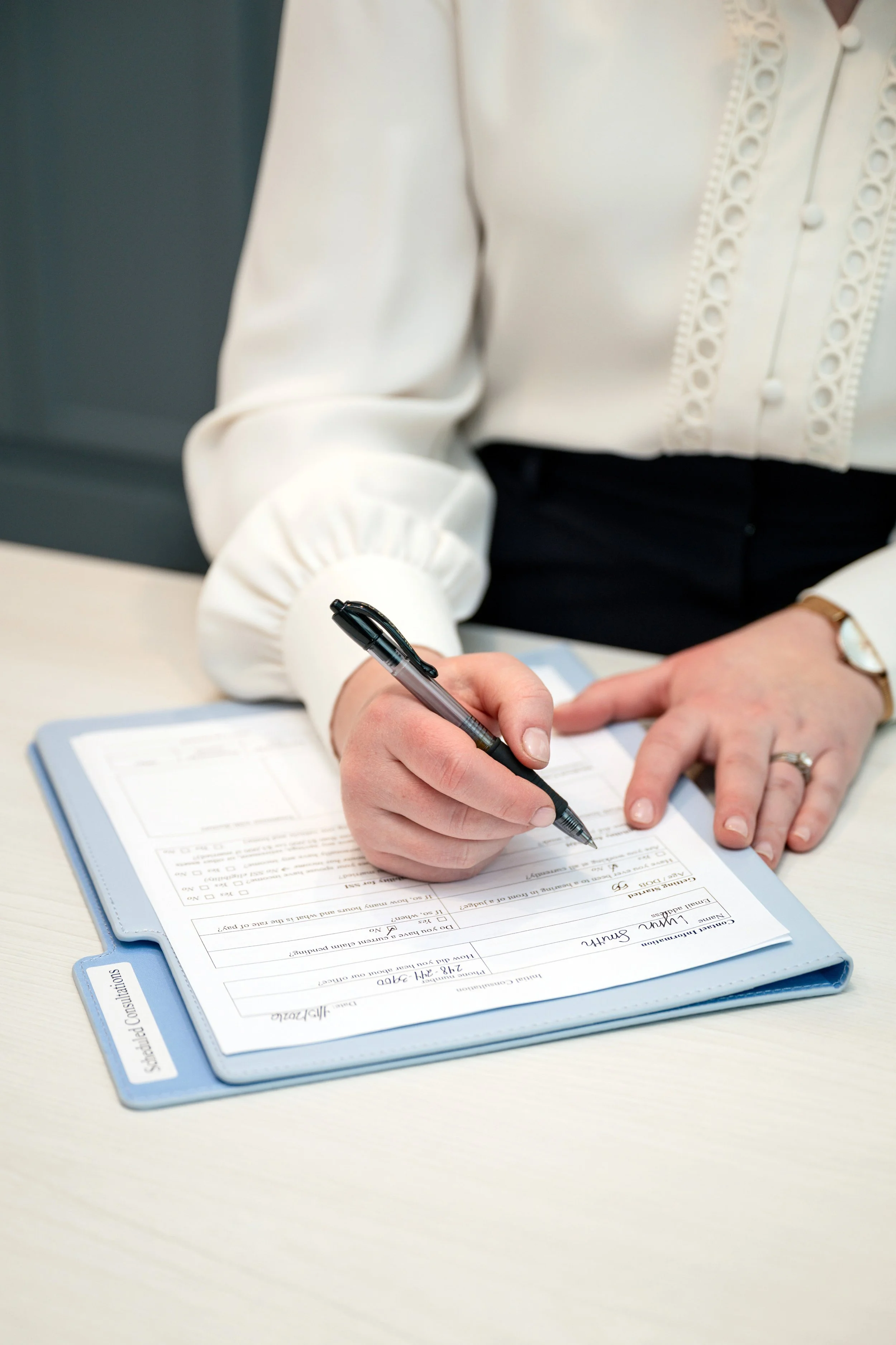 Person filling out a form on a clipboard with a pen.