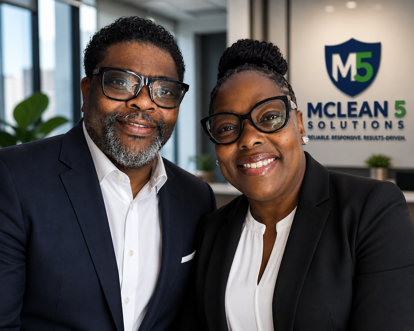 Two professionals, a man and a woman, smiling and wearing suits, standing in an office with a sign that reads 'MCLEAN 5 SOLUTIONS' in the background.