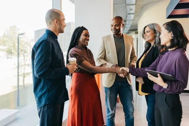 Group of five diverse professionals in business attire greeting and shaking hands in an office setting.