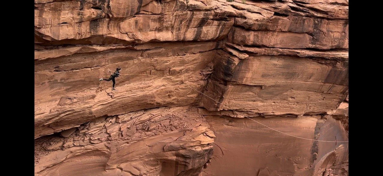 A climber's silhouette on a canyon rock wall, ropes set up for a rappel