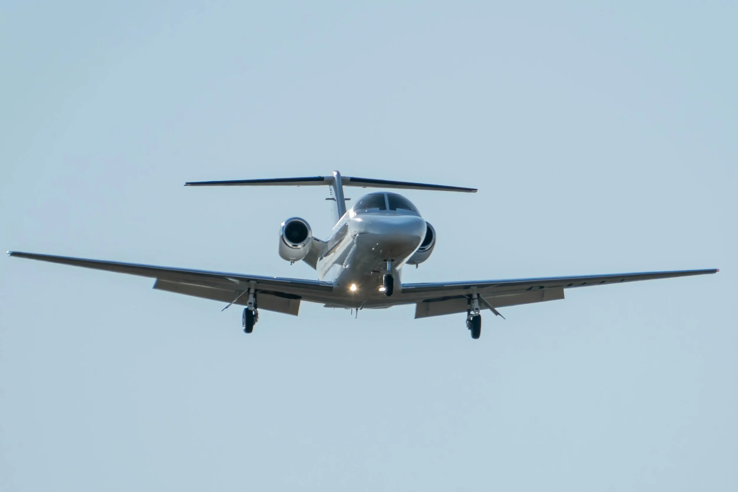 Front view of a white private jet airplane flying in a clear blue sky.