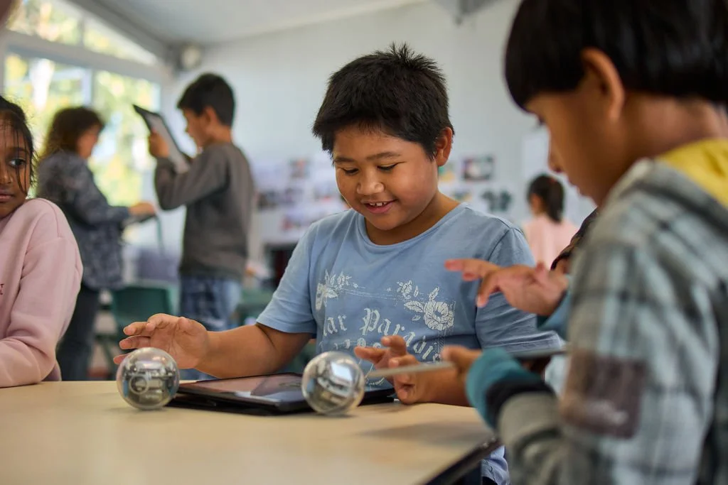 Children in a classroom playing with small robots and tablets.