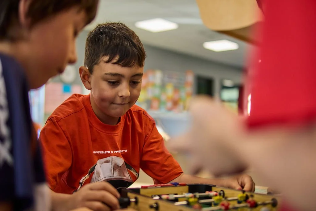 Children playing foosball in a classroom or play area.