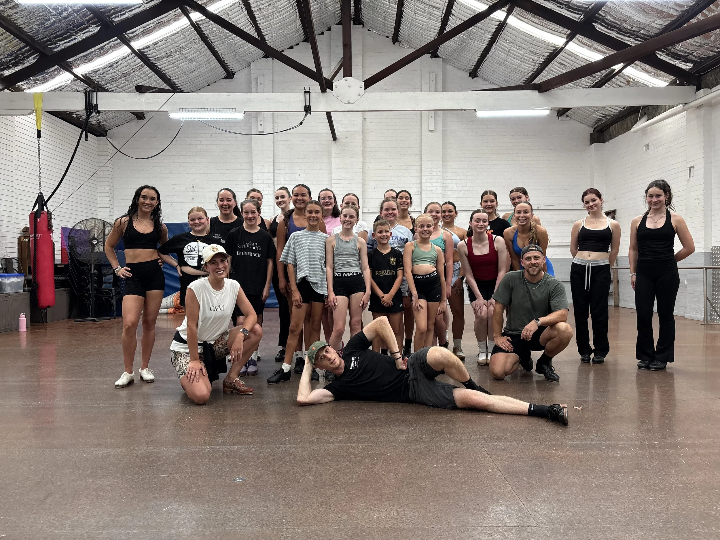 Group of children and adults in a gymnasium, wearing athletic clothing, posing for a photo after a workout or dance class.