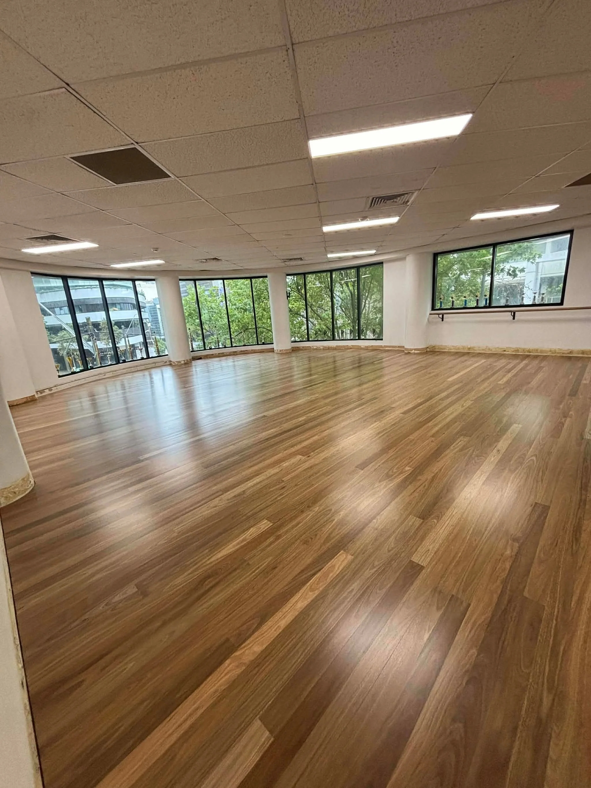 Empty room with large windows, hardwood flooring, and a white ceiling with fluorescent lights.