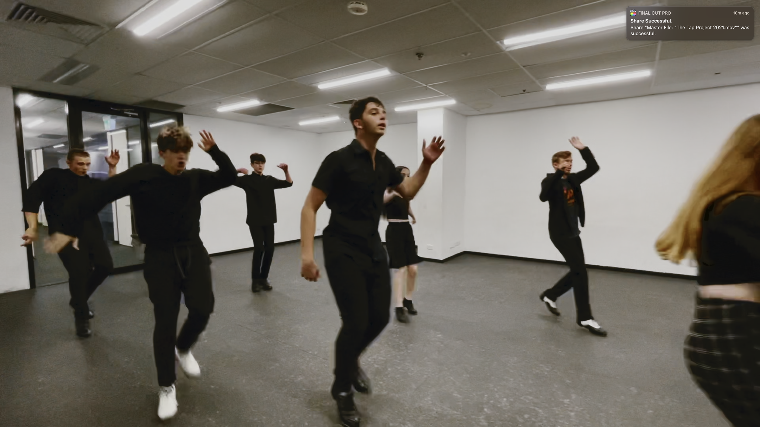 Group of young men dancing in a room with white walls and ceiling lights.