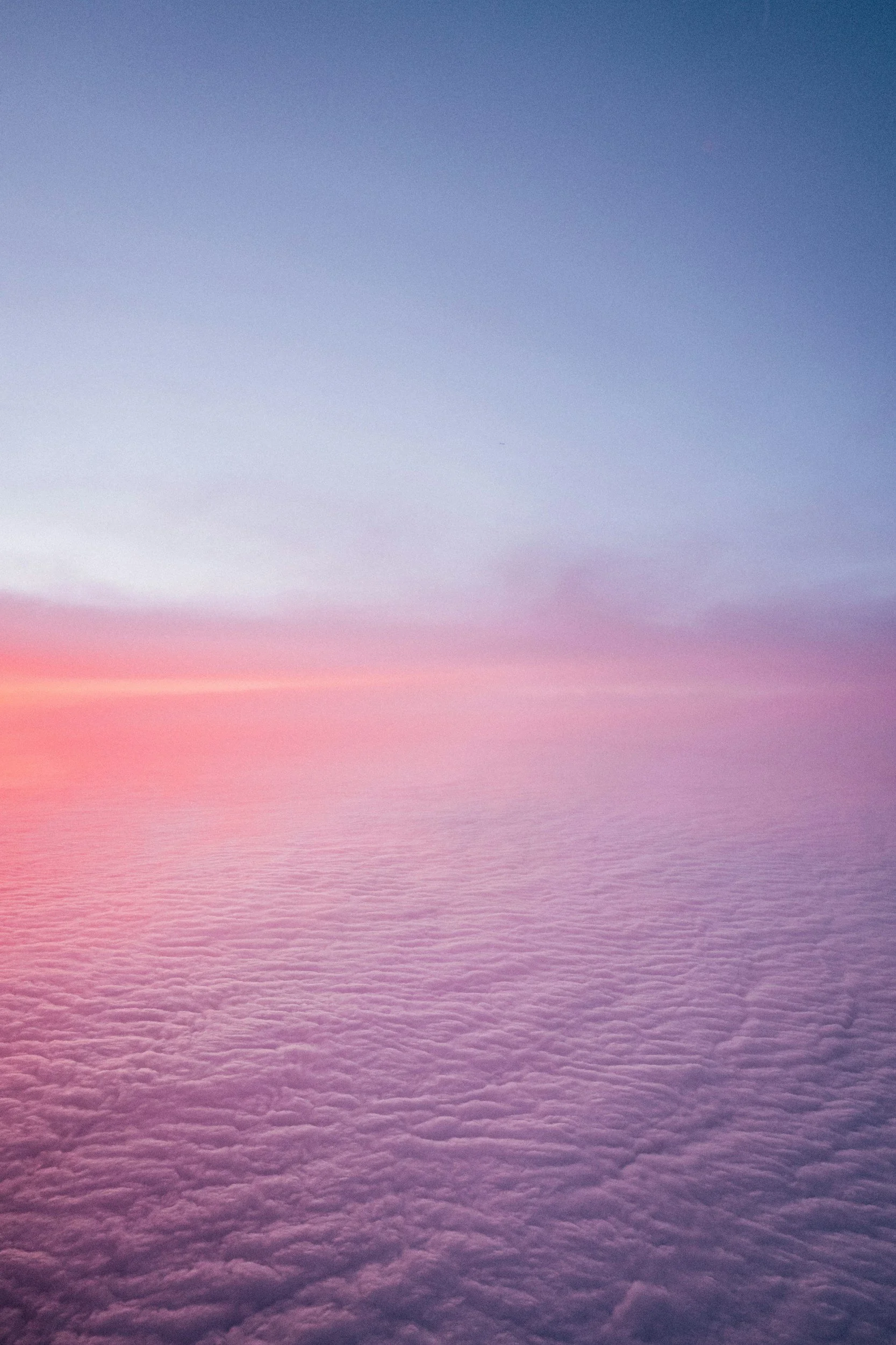 A view of the sky from above the clouds during sunset, with shades of pink, purple, and blue.
