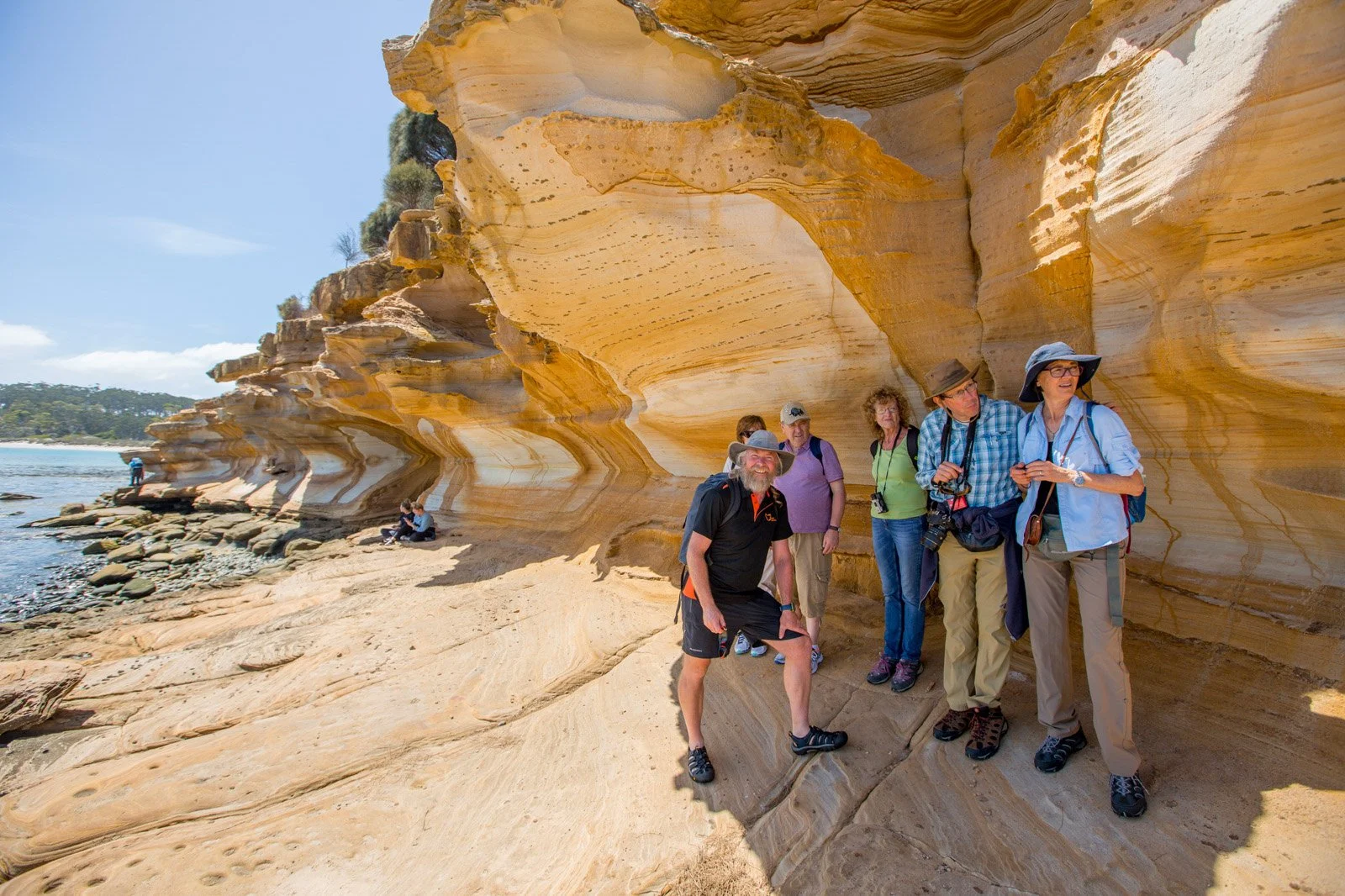 The famous painted cliffs at Maria Island, with Tours Tasmania guide and day tour group standing behind him.
