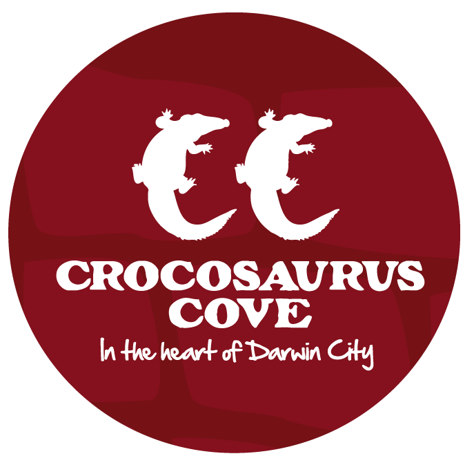 Logo for Crocosaurs Cove, featuring two white crocodile illustrations, with the text "Crocosaurs Cove" and "In the heart of Darwin City" on a red circular background.