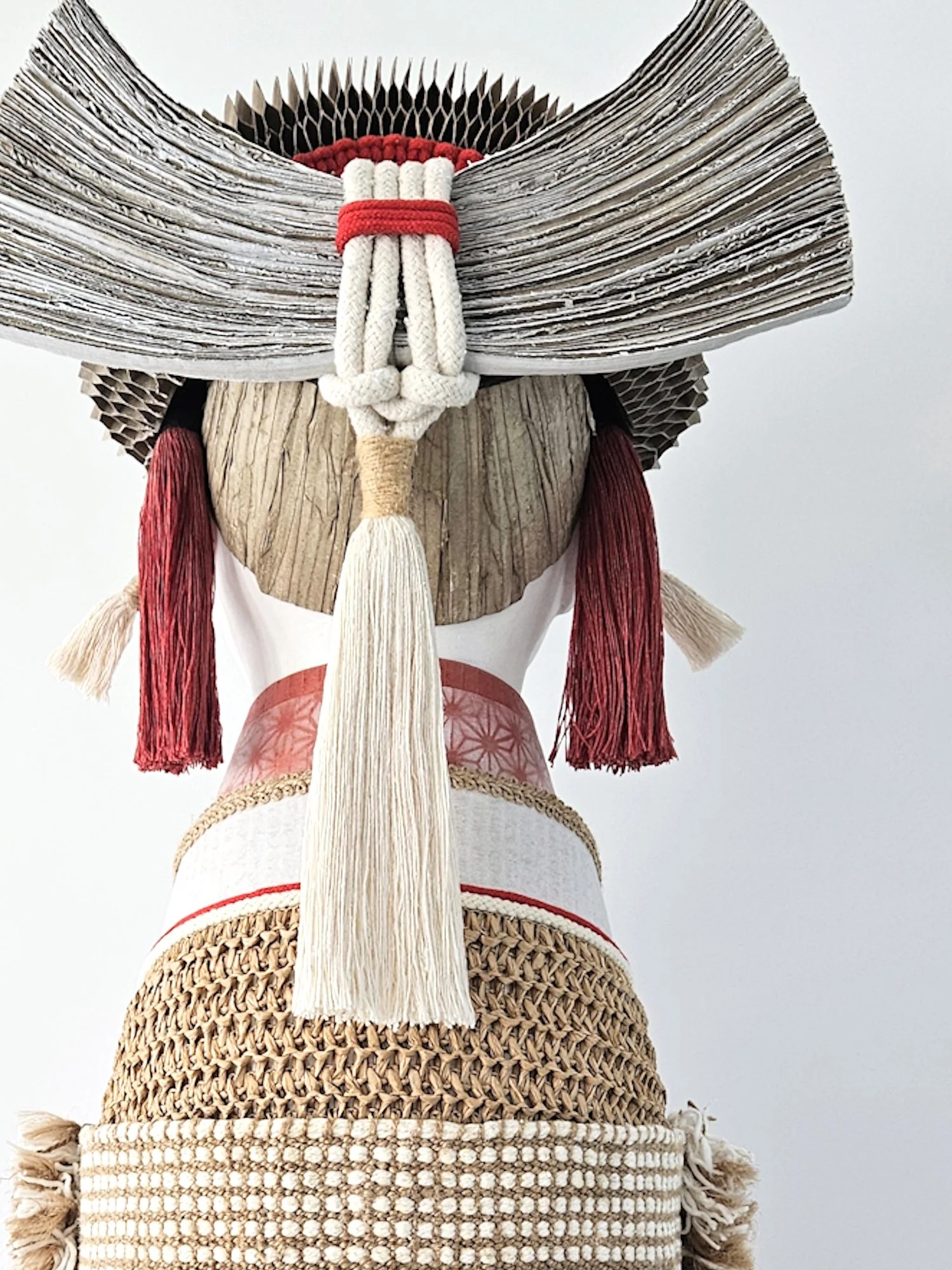 Close-up of a Japanese inspired sculpture, dressed in a kimono with an elaborate wide-brimmed cardboard headpiece. The face is not visible, and the focus is on the detailed patterns and textures of the headpiece and clothing.