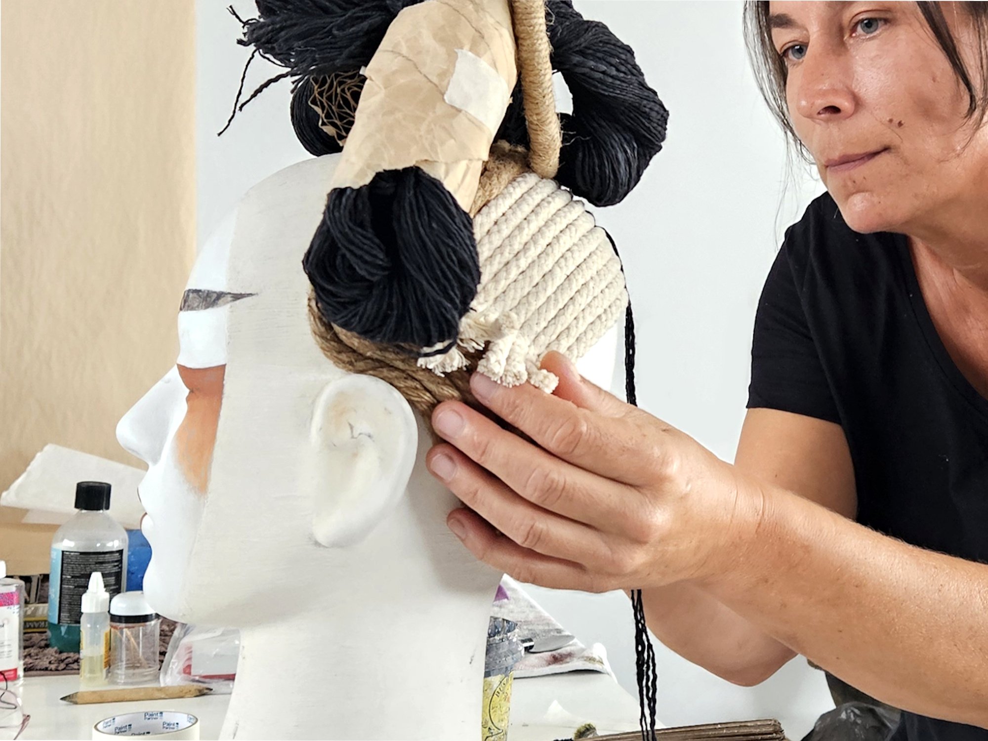 An artist holding a sculpture or art piece made of yarn and other materials.