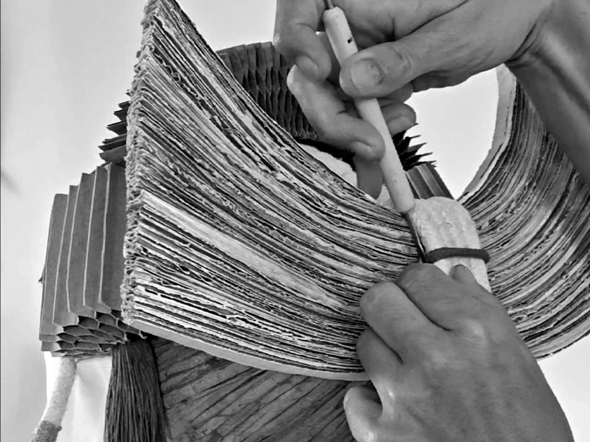 A person's hand holding a tool and working on an intricate headpiece made from cardboard with multiple layered sections.