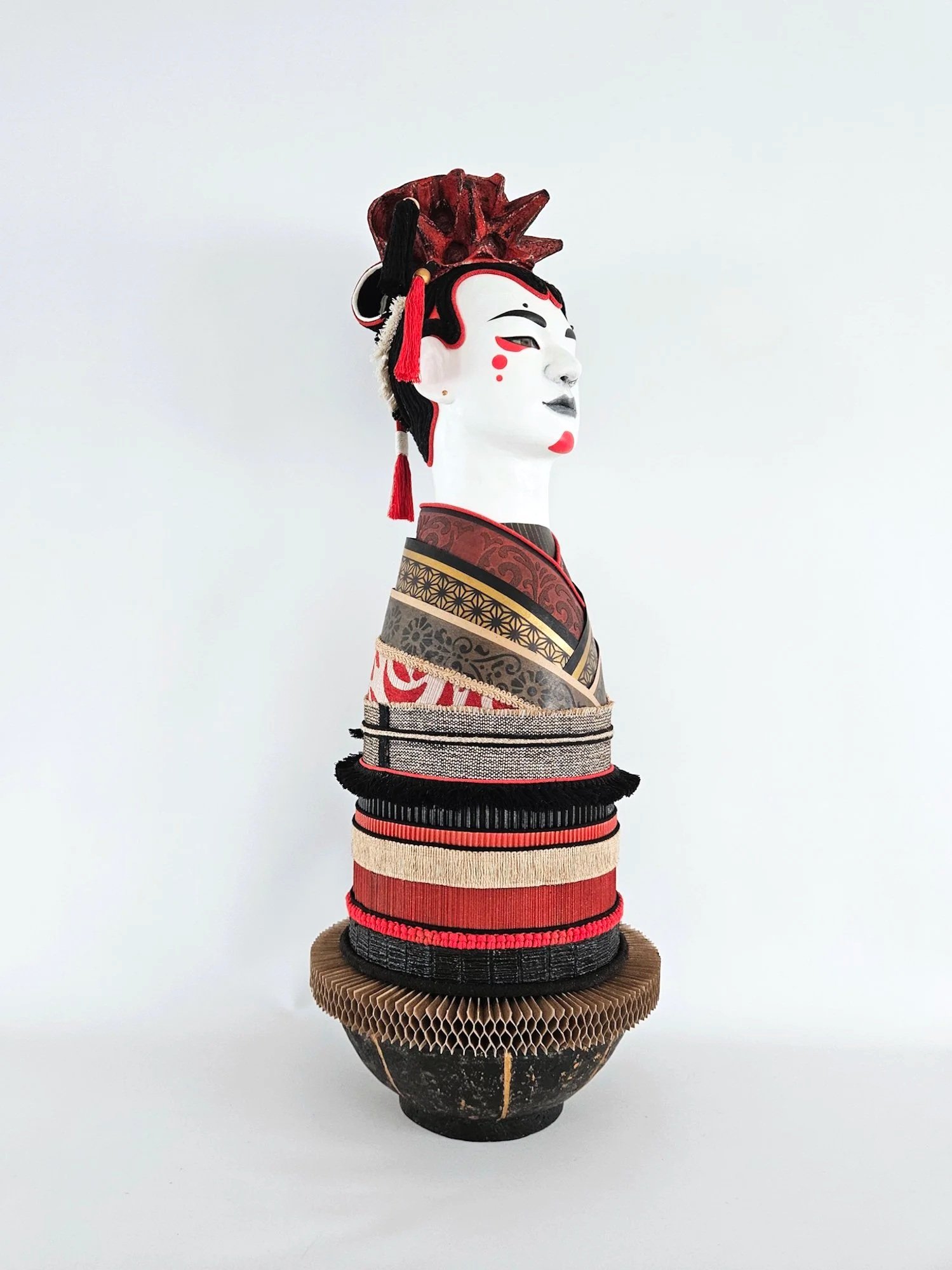 A Japanese Noh theater inspired sculpture, layered fabric and paper, decorated with intricate patterns and red accents.