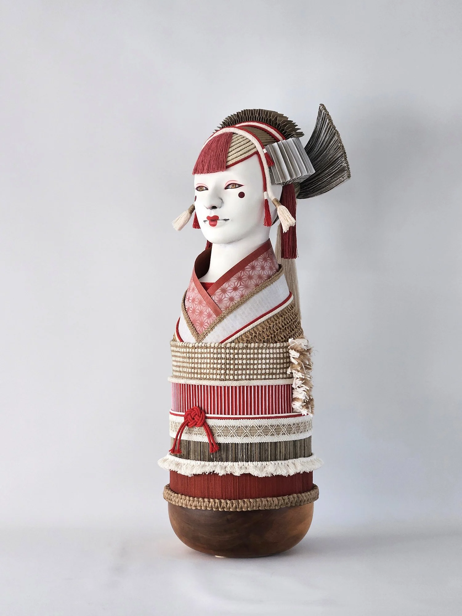 A Japanese inspired sculpture with elaborate decorative elements and multiple layers of fabric, placed on a wooden stand.