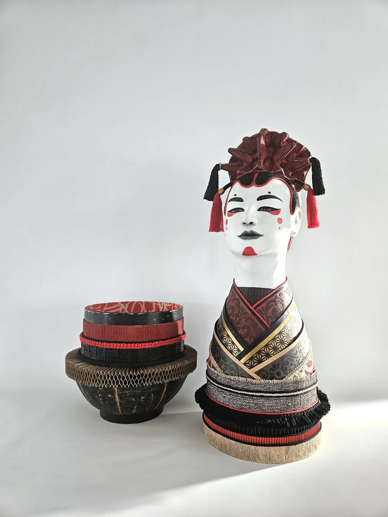 Two traditional Japanese decorative , one on top of a black and red lacquered box, with a backdrop of a plain, light-colored wall.