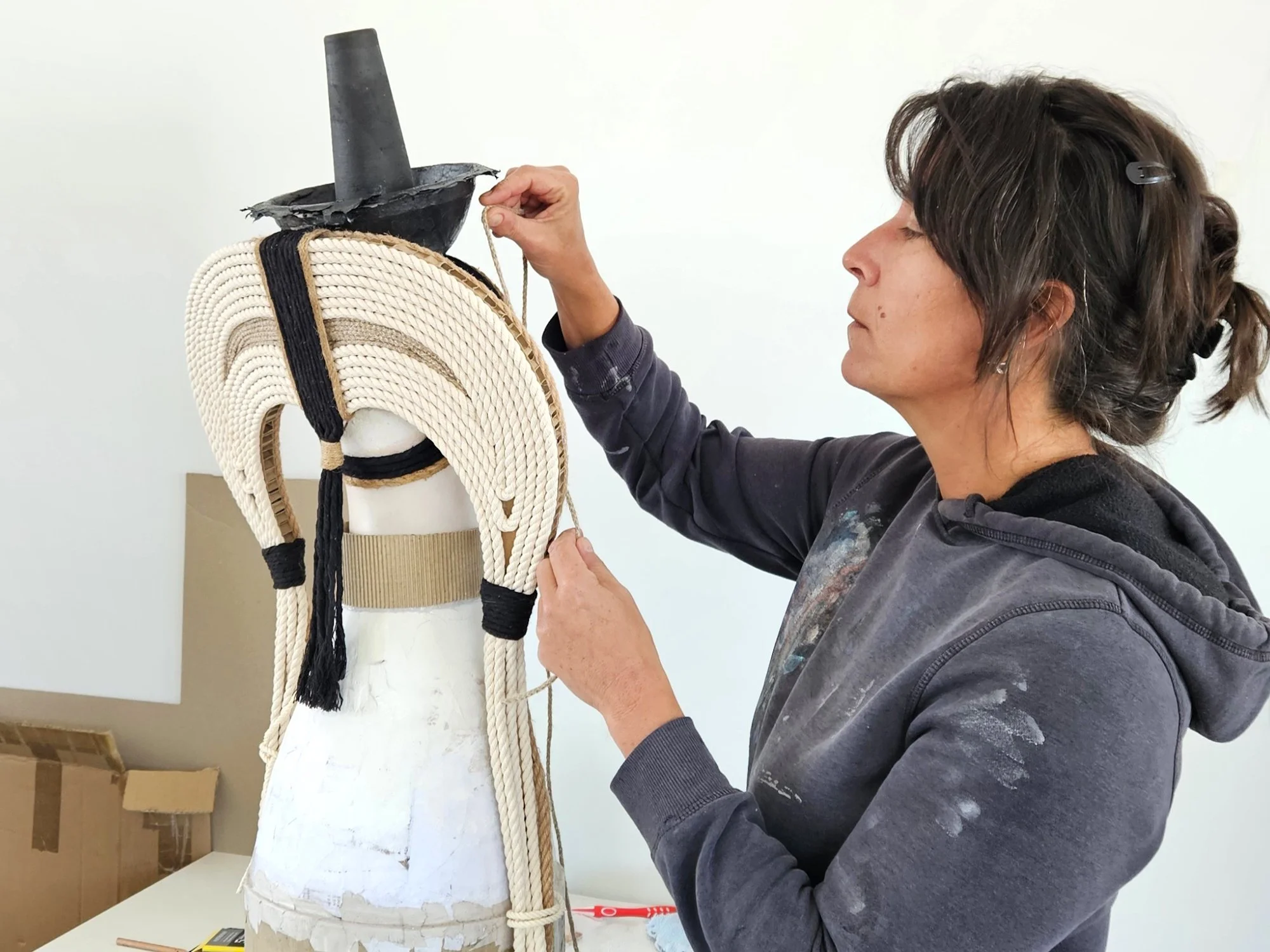 An artist working on a sculpture, in a studio setting with a plain white wall.