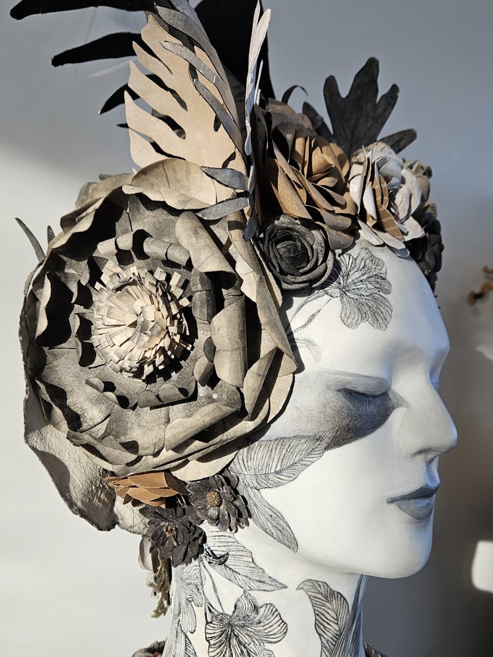 A head sculpture decorated with paper flowers, leaves, and intricate designs, creating a floral headdress and face embellishments.