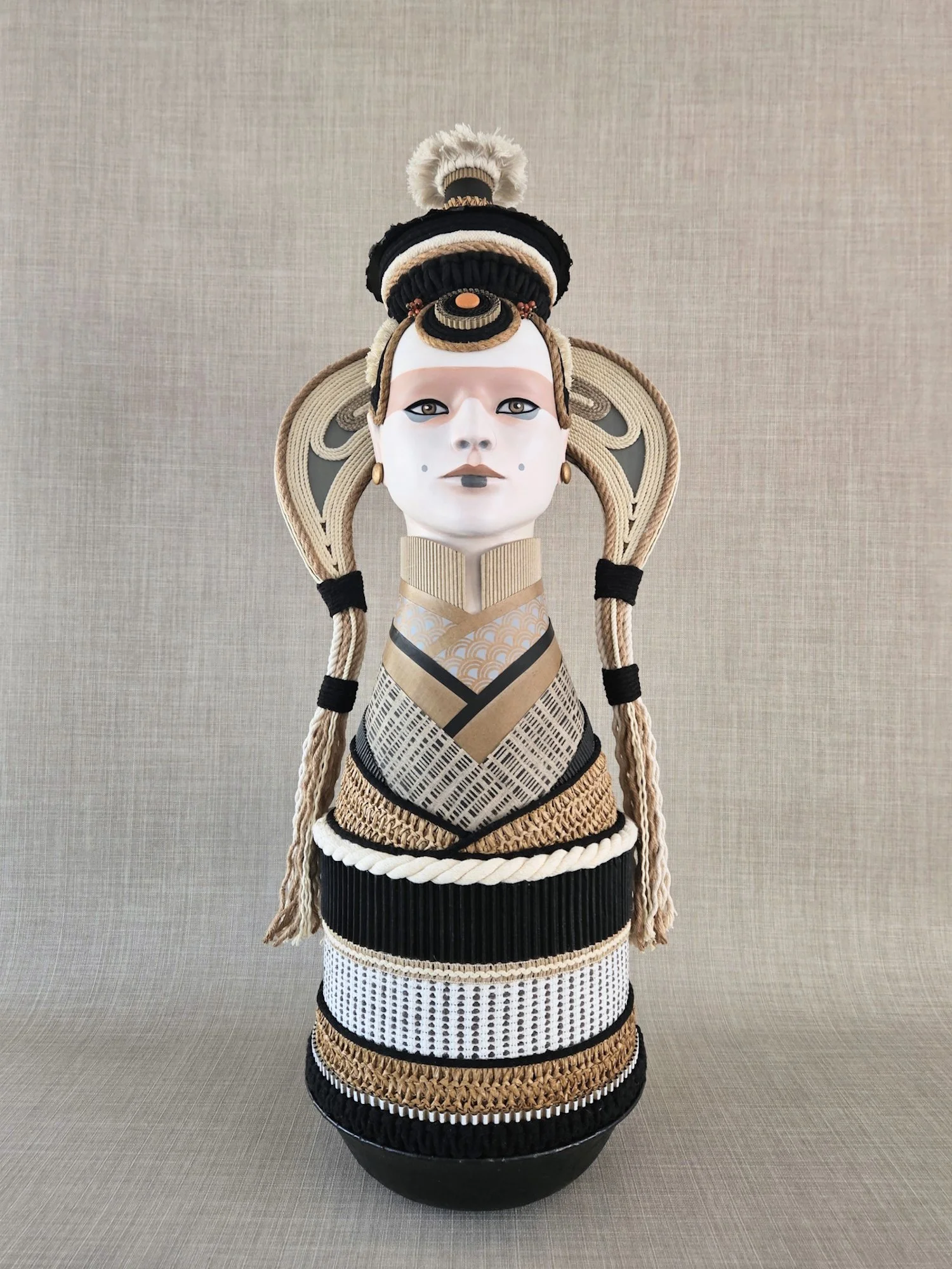 A tall decorative sculpture of a woman with elaborate hair and traditional clothing, made from woven and textured materials in black, beige, and white.