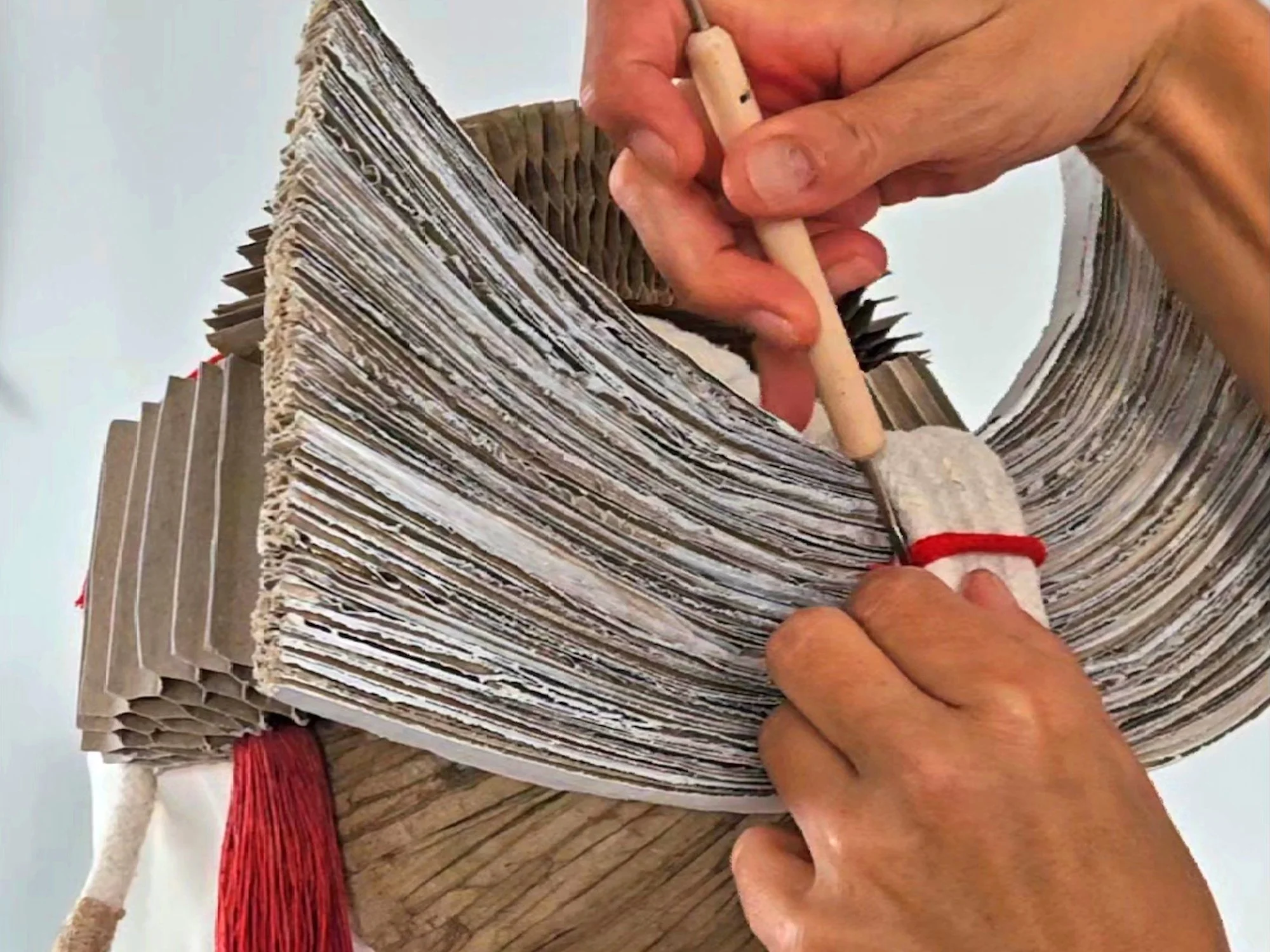 Close-up of hands carving or sculpting a large structure made of paper, cardboard, or a similar material, with architectural or artistic design details.