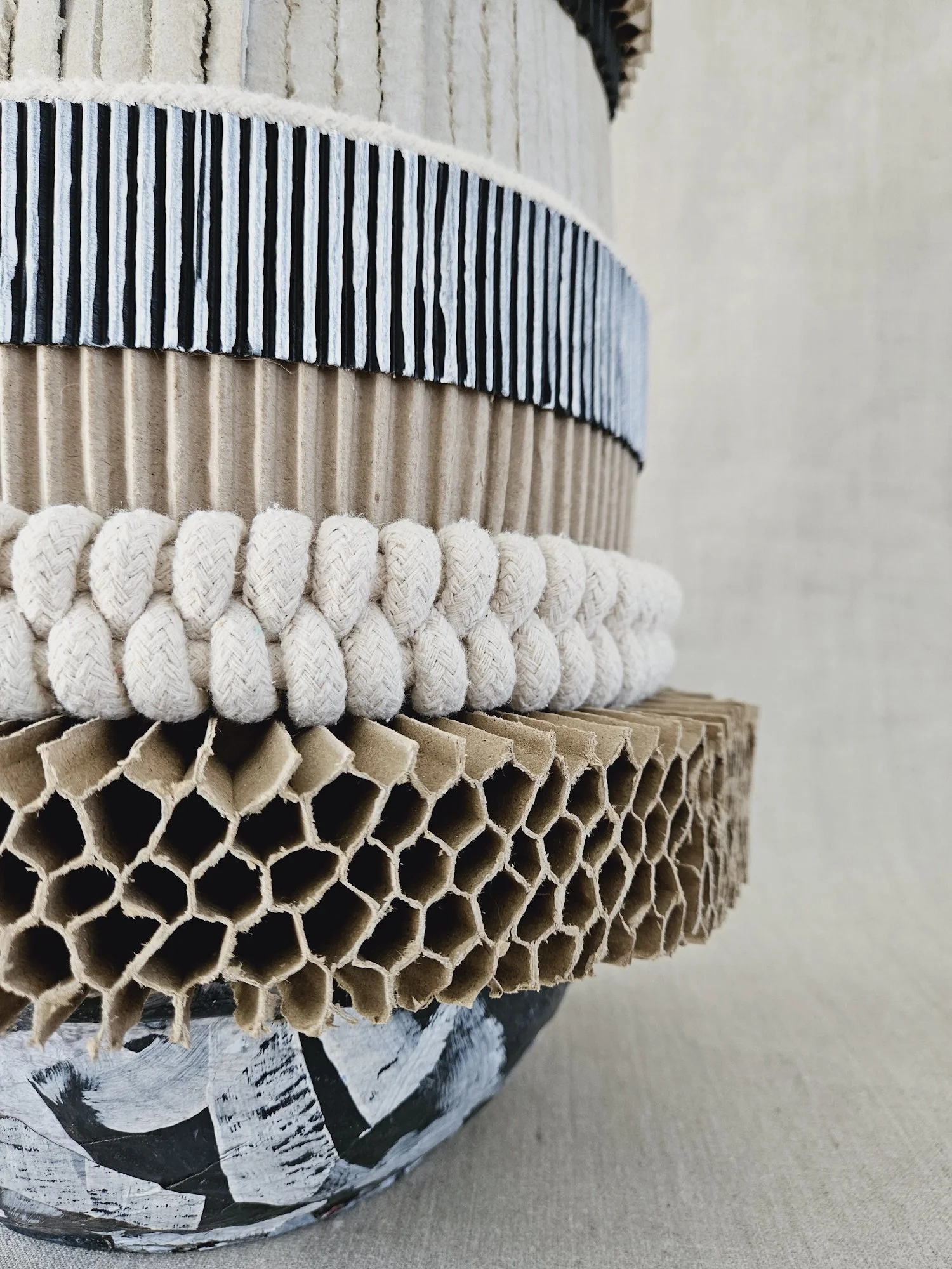 Close-up view of stacked cardboard tubes and paper craft materials, including paper with black and white abstract design, a knitted rope, and bakery cups with striped paper liners.