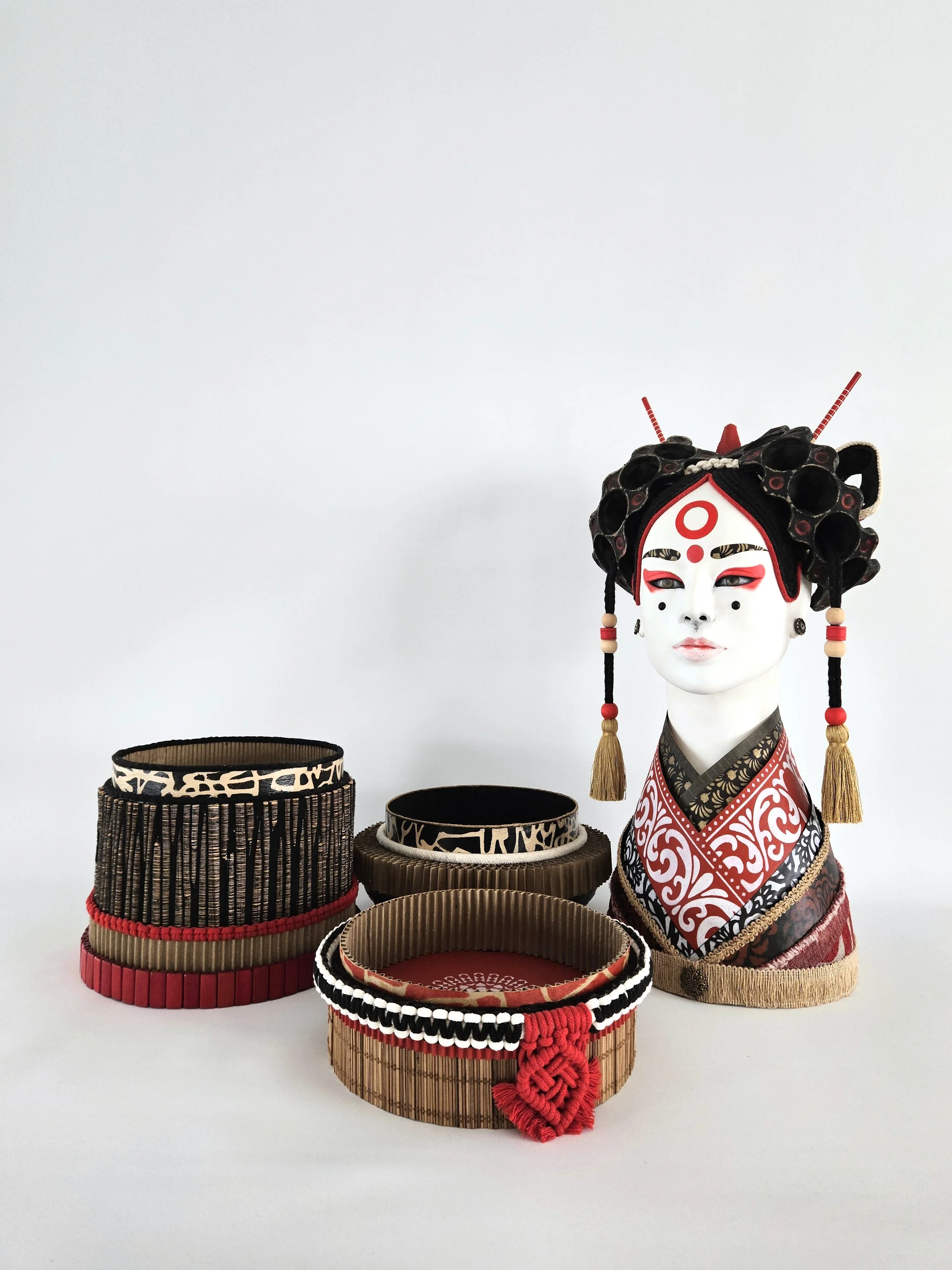 Asian inspired sculpture of a geisha with an elaborate headdress and makeup, set against a plain white background.