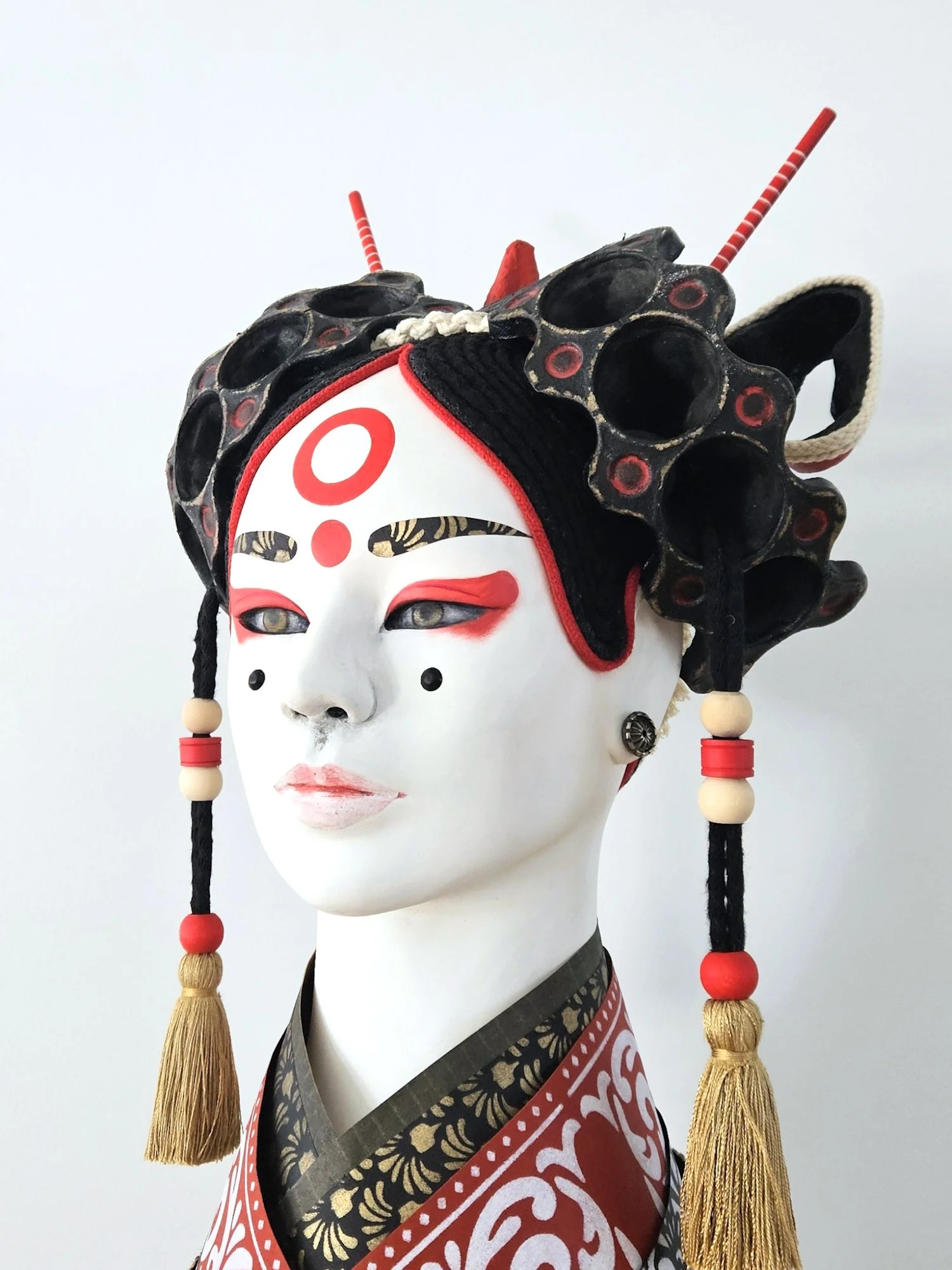 A traditional Japanese mask with elaborate headdress and costume, featuring white face paint, red accents, and tassels.