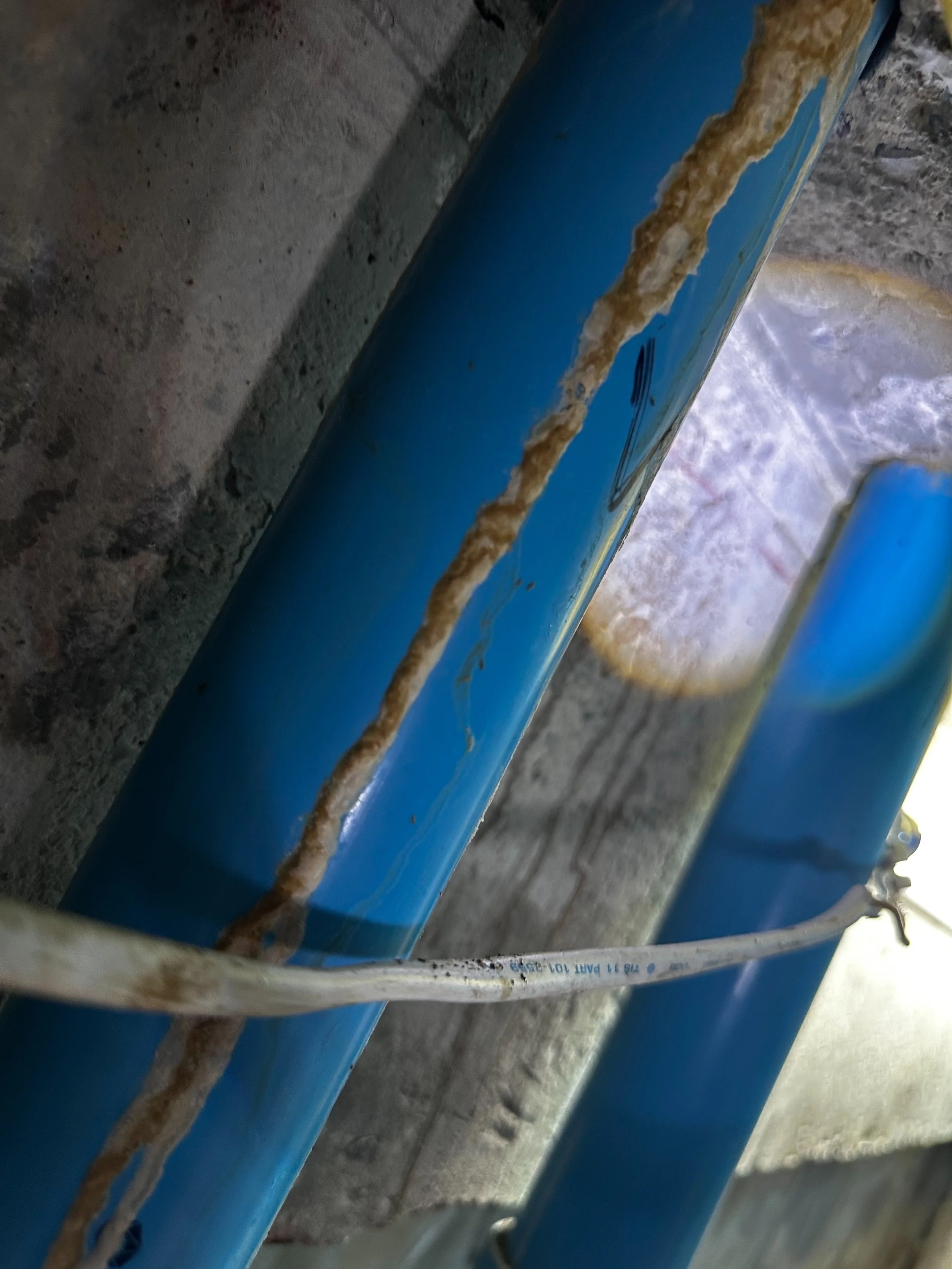 Close-up of blue painted metal pipes with rust and dirt, positioned against a concrete surface.