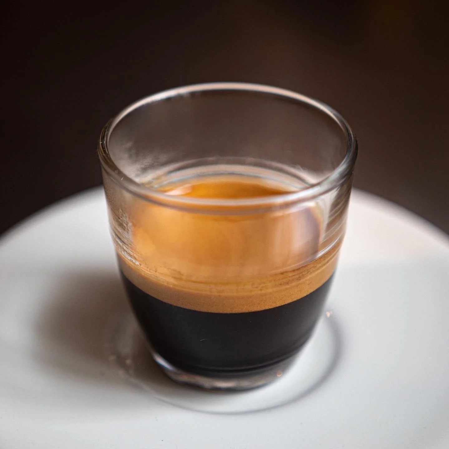 A small glass of dark espresso coffee on a white plate.